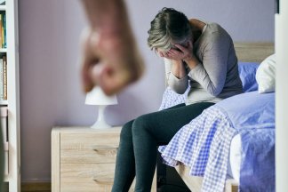 Žena sedící na posteli se obává fyzického napadení