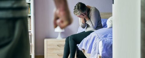 Žena sedící na posteli se obává fyzického napadení
