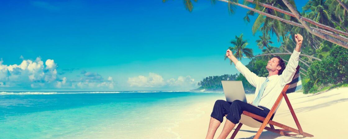 Muž s počítačem sedí na pláži na lehátku