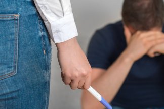 žena v popředí zdrceného muže drží v ruce těhotenský test