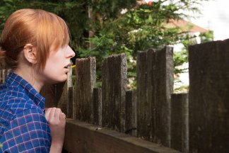Žena stojící u vysokého plotu se dívá na sousedovu zahradu