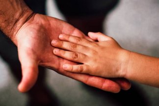 Ruce malého dítěte a otce řešícího náhradní výživné