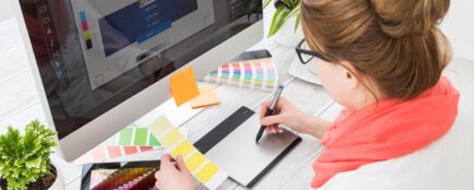 Žena sedící před počítačem zkouší barevné kombinace se vzorníkem