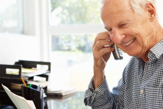 Starší muž telefonuje u svého pracovního stolu