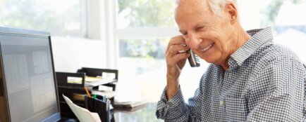 Starší muž telefonuje u svého pracovního stolu